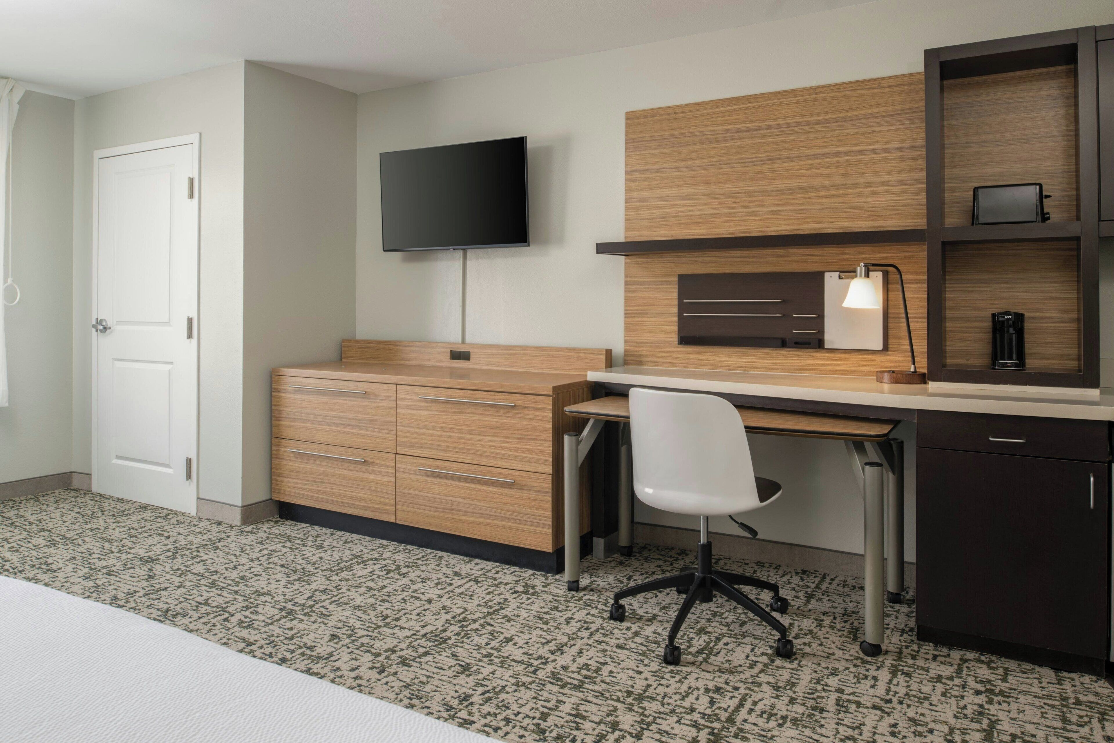 A modern bedroom with a bed, a desk with a chair, a TV, and a wardrobe.
