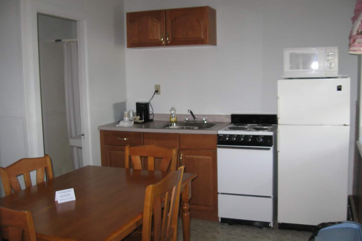 A compact kitchen with wooden cabinets, a white refrigerator, a stove, and a microwave.