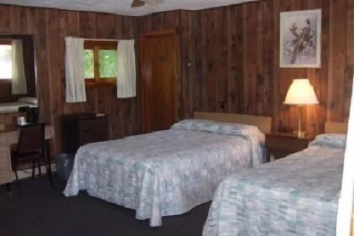 A room with two beds, a desk, a chair, and a lamp.