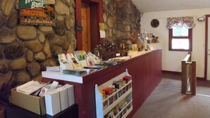 Un área de recepción con pared de piedra, mostrador de madera, un letrero del Motel Moose Brook y una ventana con cortina.