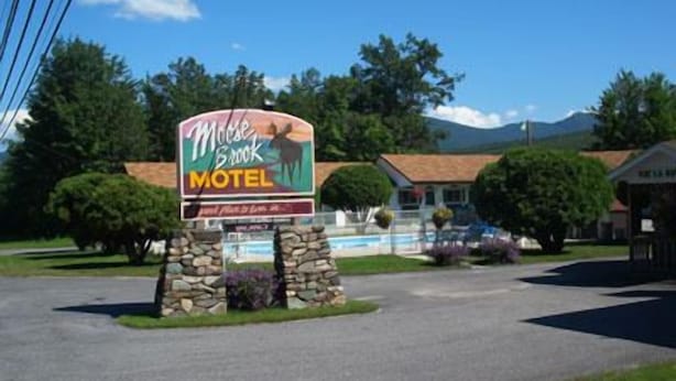 Un letrero de motel con un gráfico de alce, rodeado de pilares de piedra y jardines.