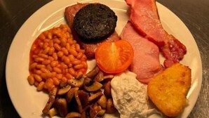 Un plato de comida con frijoles, champiñones, una rodaja de tomate, morcilla, tocino y una patata frita.