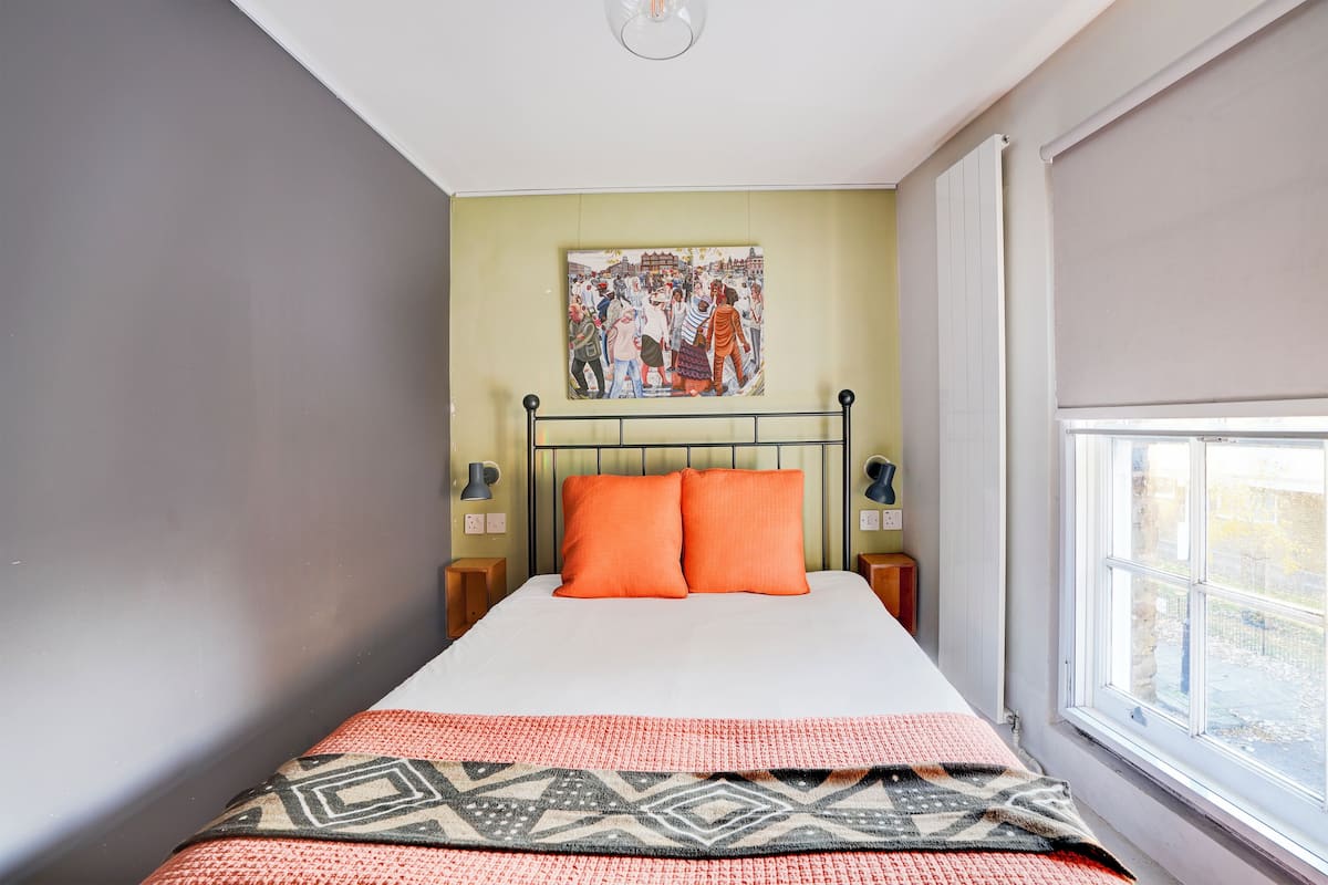 A bedroom with a bed, a painting on the wall, and a window.