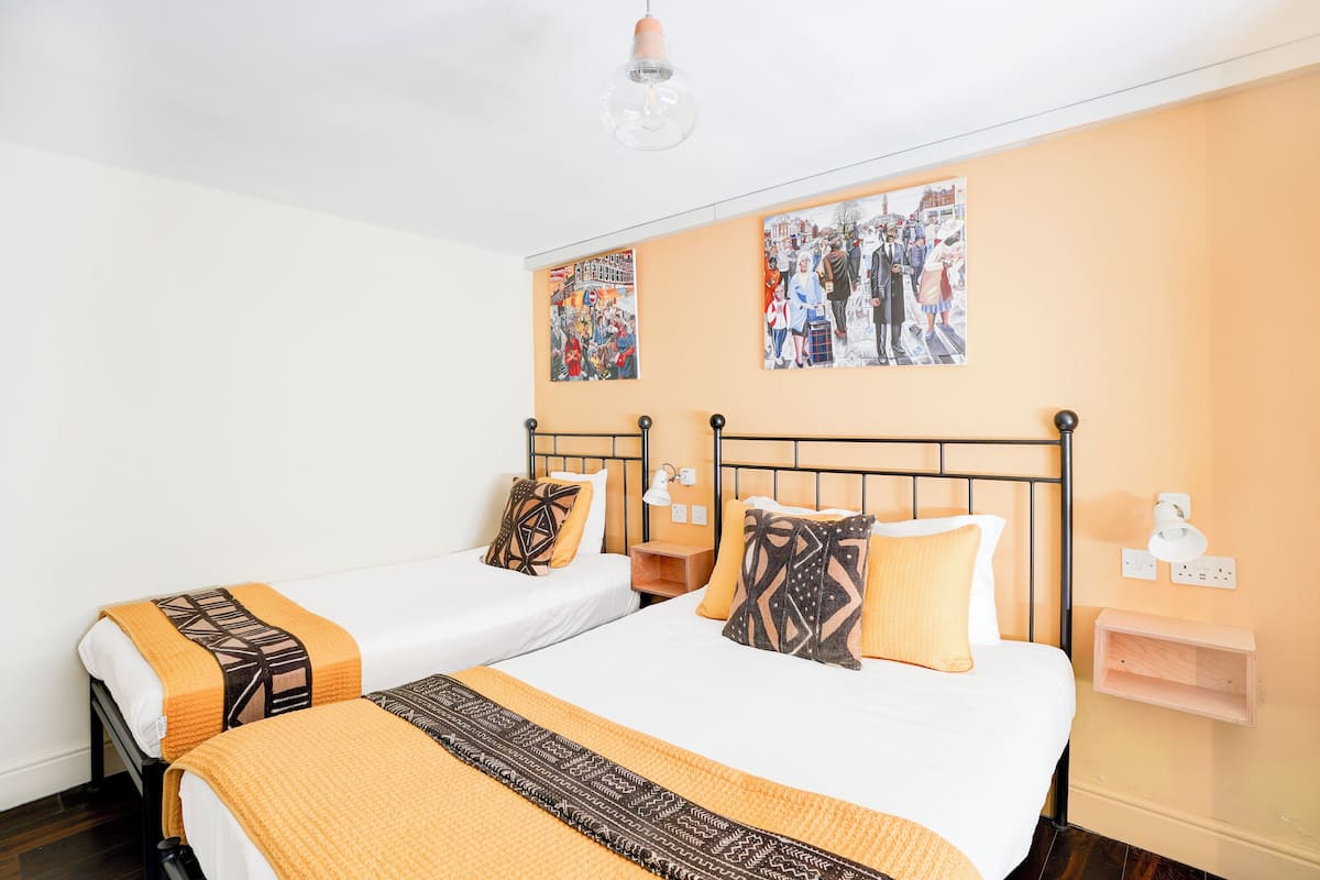 A hotel room with two beds, each with patterned bedspreads and pillows, a wall-mounted shelf, and two wall-mounted light fixtures.
