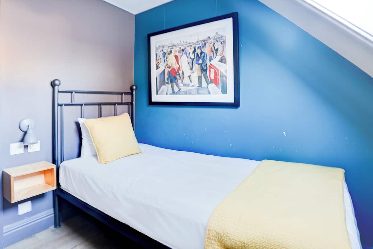A bedroom with a bed, a nightstand, a wall-mounted lamp, and a framed picture.