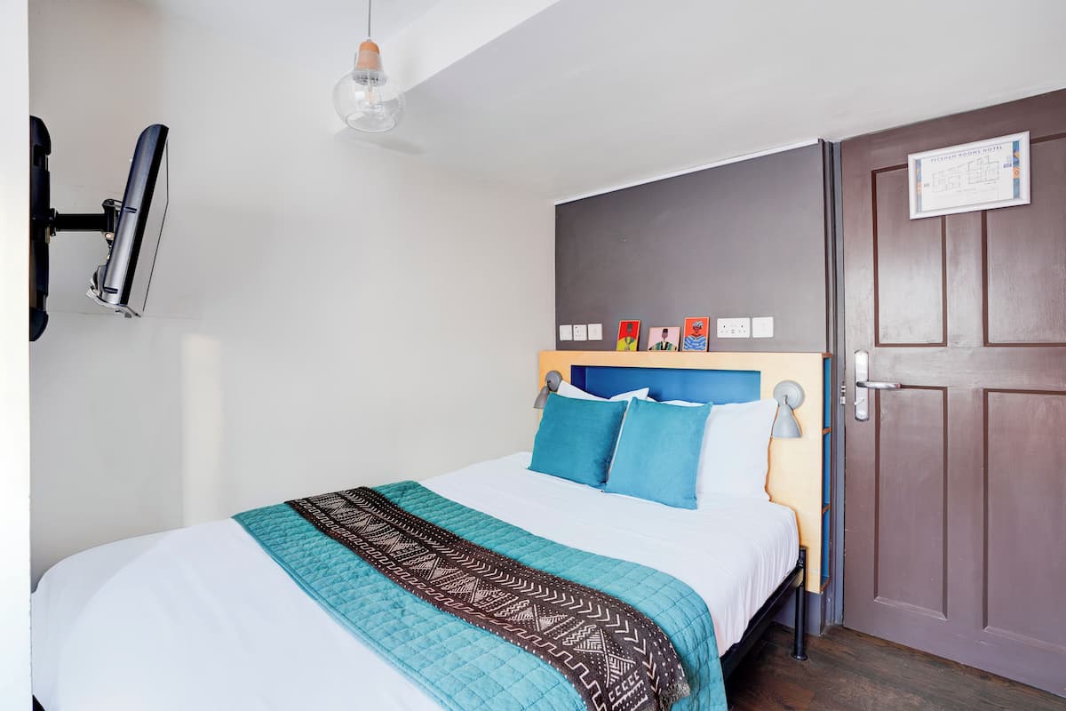 A neatly made bed with a patterned blanket, a headboard with a plaque, and a bedside lamp.