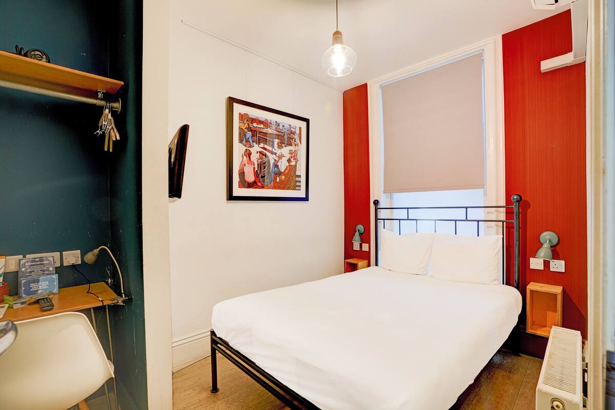 A bedroom with a bed, bedside tables, a desk with a chair, a hanging light fixture, and a framed picture on the wall.