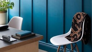 Una zona de recepción con pared verde azulado, un escritorio, una silla y una planta en maceta.