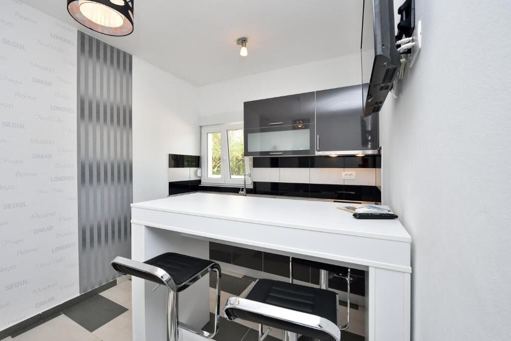 Een moderne keuken met een wit aanrecht, zwarte kasten en roestvrijstalen apparatuur. Er staan twee barkrukken met zwarte zittingen en chromen poten.