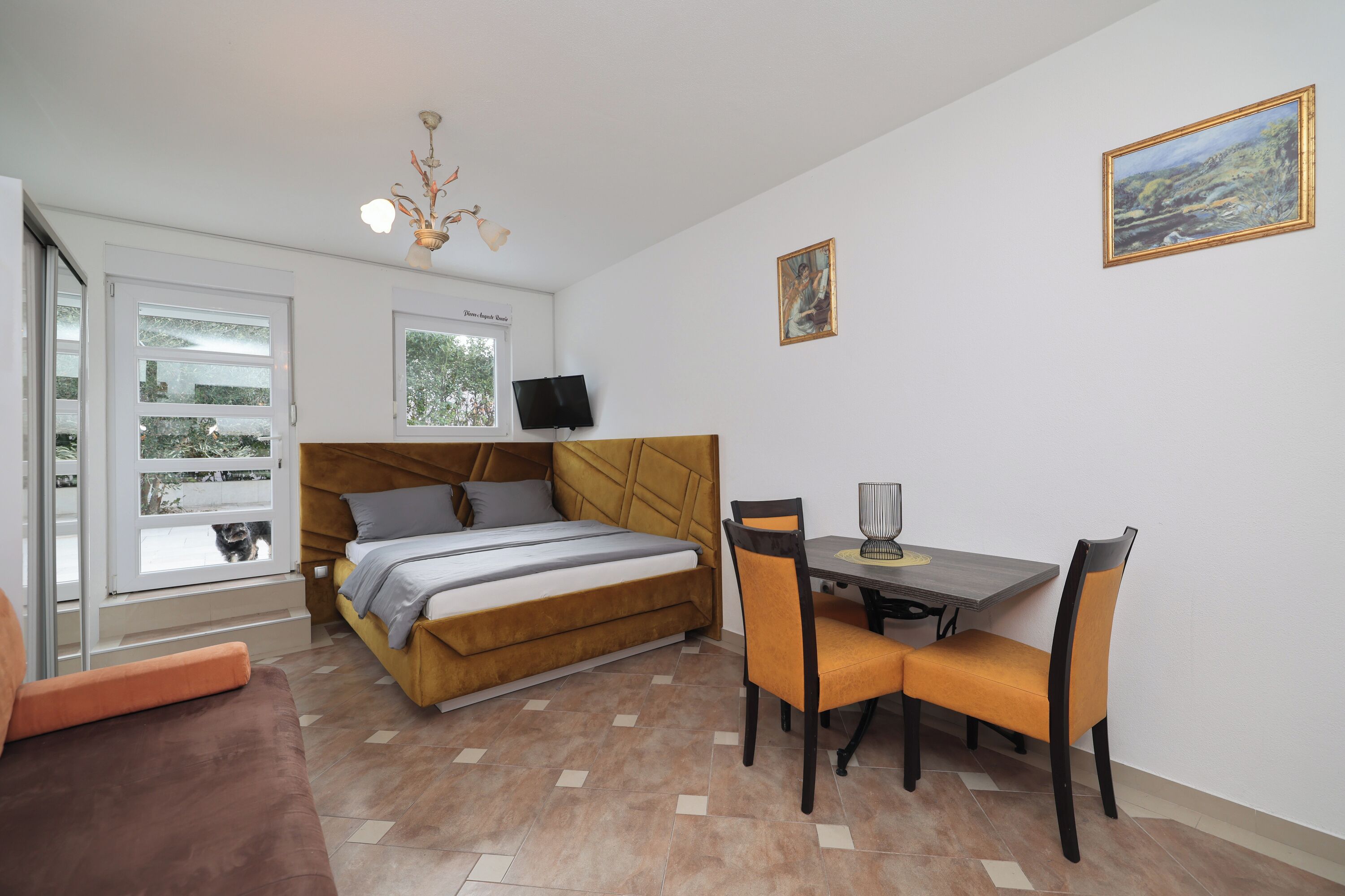 A bedroom with a bed, a desk, and chairs, a television, and a window with a view of trees.