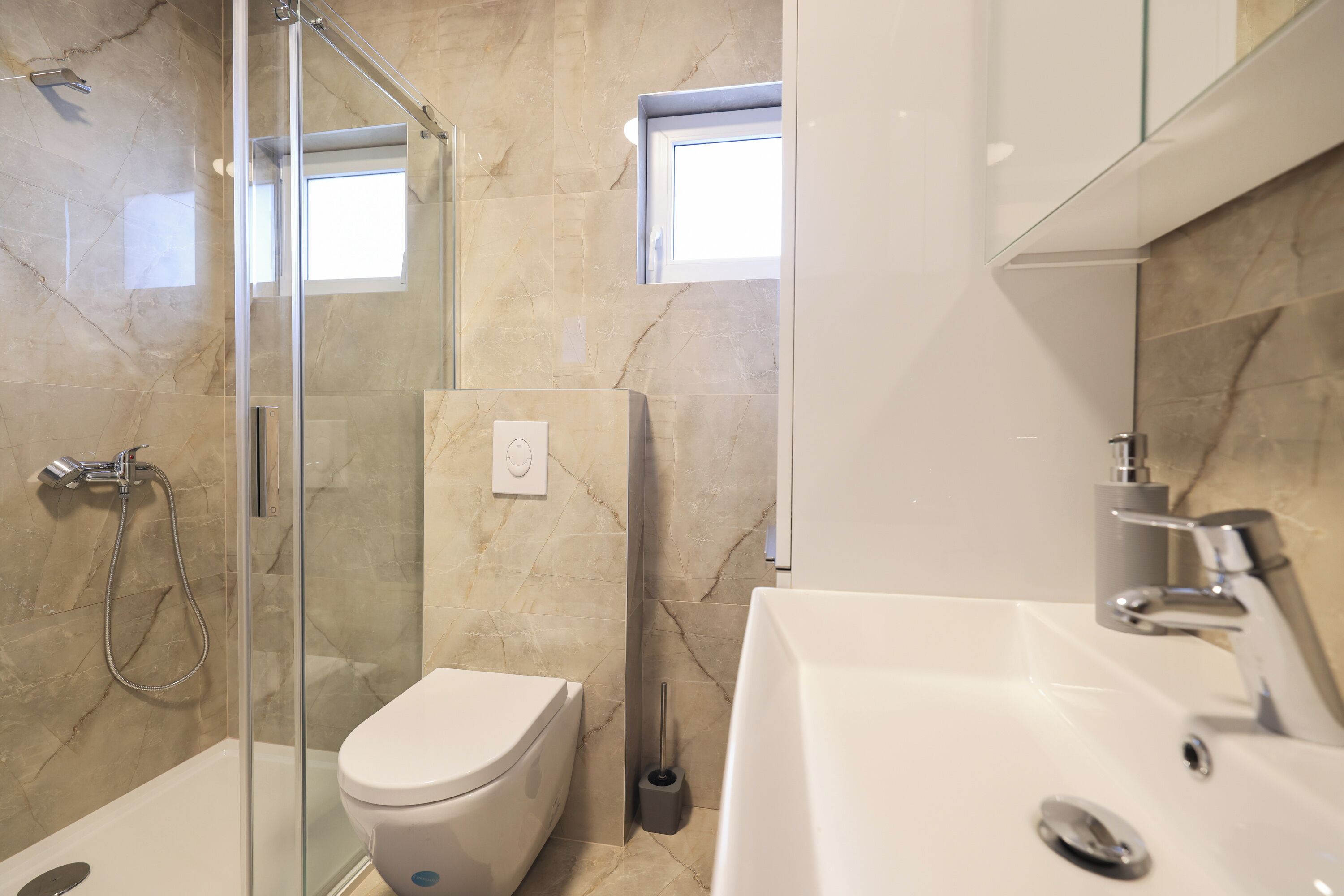 Une salle de bain moderne avec une douche à parois de verre, des toilettes et un lavabo surmonté d’un miroir.