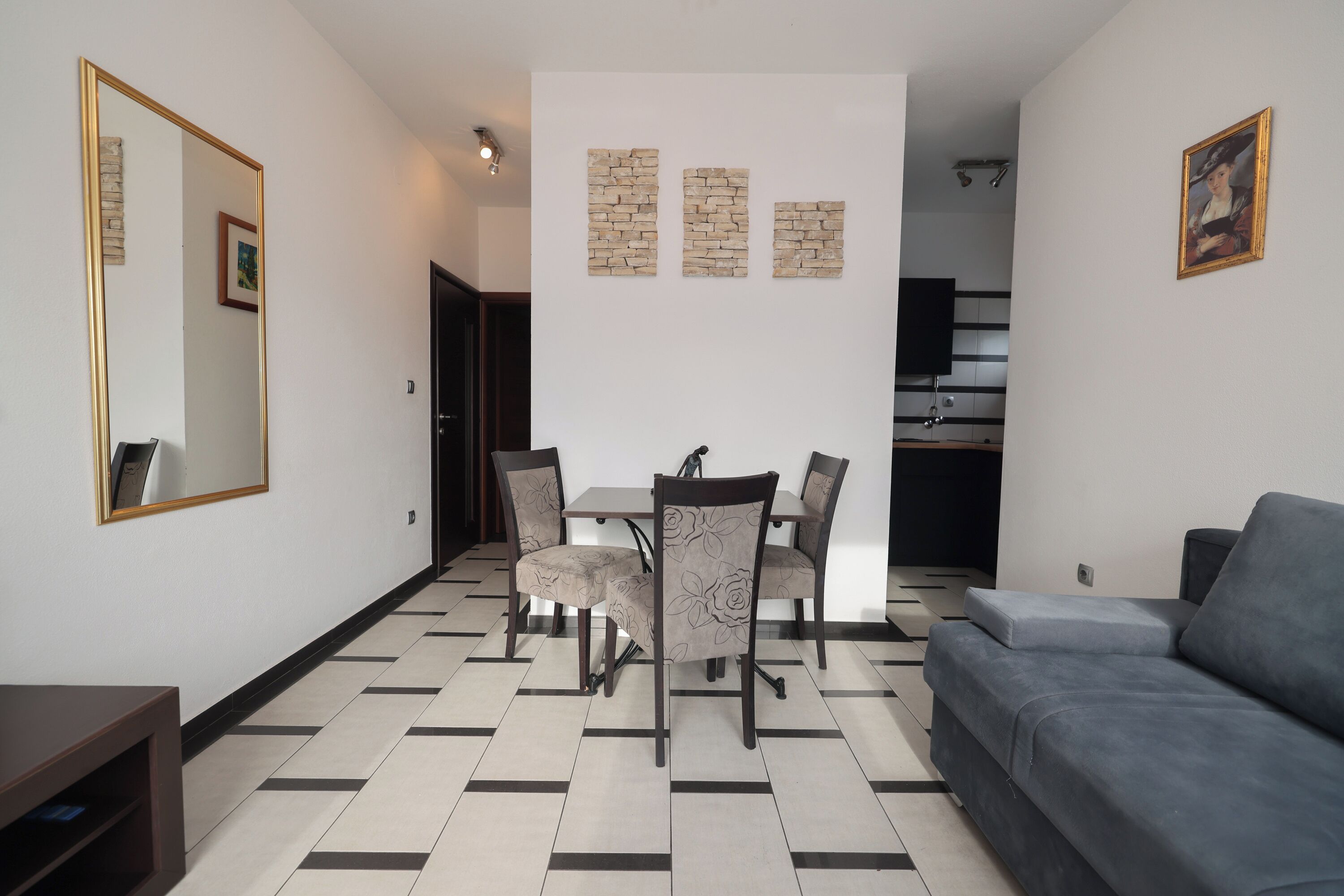 Una sala de estar con un sofá gris, una mesa de comedor con cuatro sillas, un espejo grande y tres obras de arte colgadas en la pared.