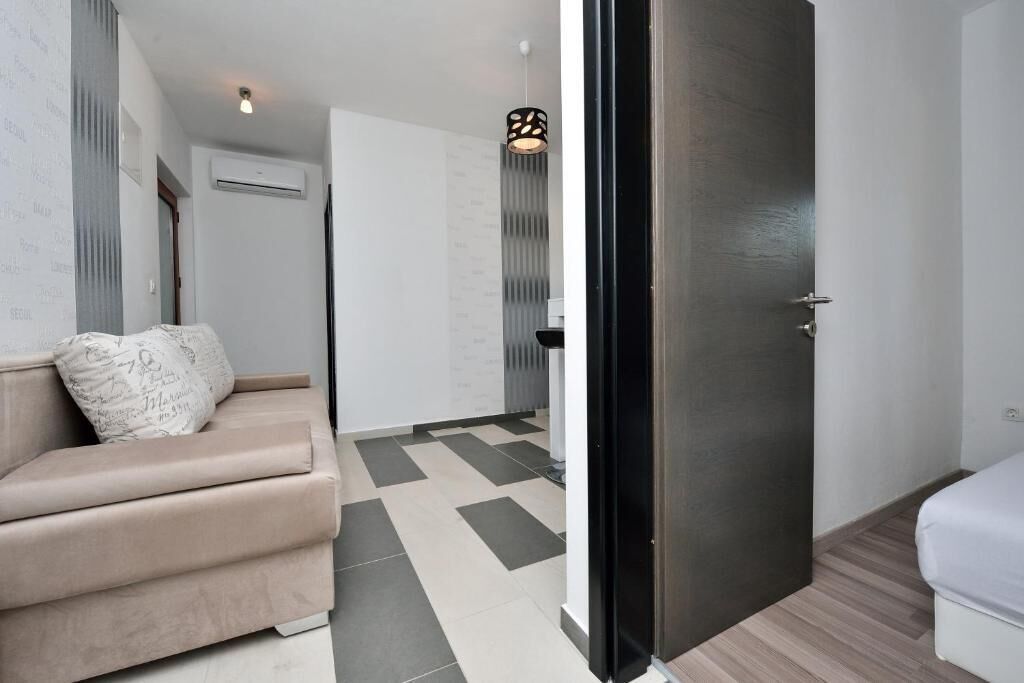 A modern hotel room with a beige sofa, a black door, and a checkered floor pattern.