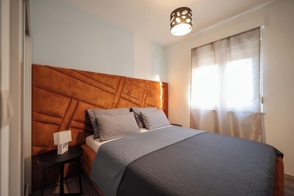 A bedroom with a large bed, a headboard, a bedside table, and a lamp.