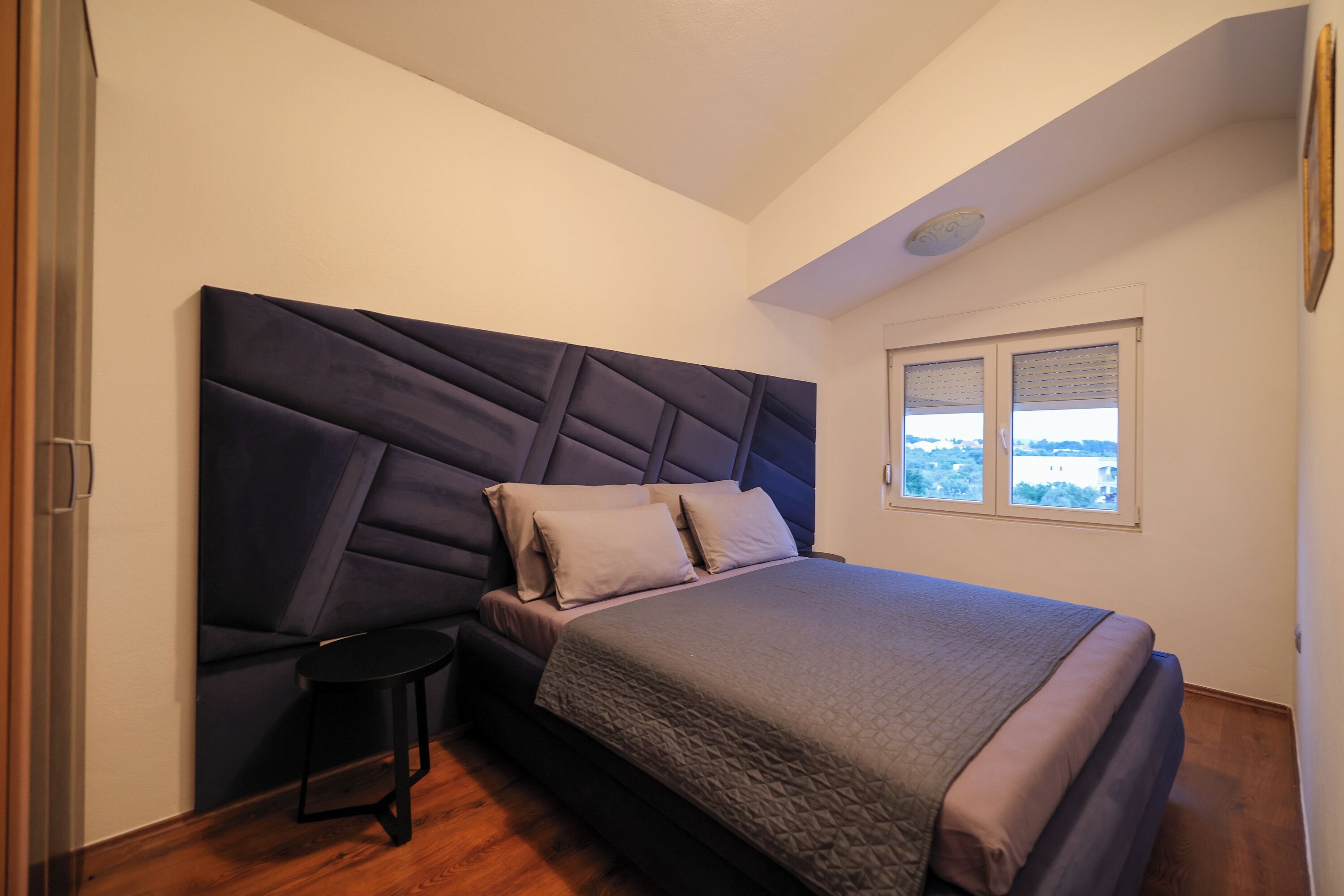 A bedroom with a large bed, a nightstand, and a window with a view.