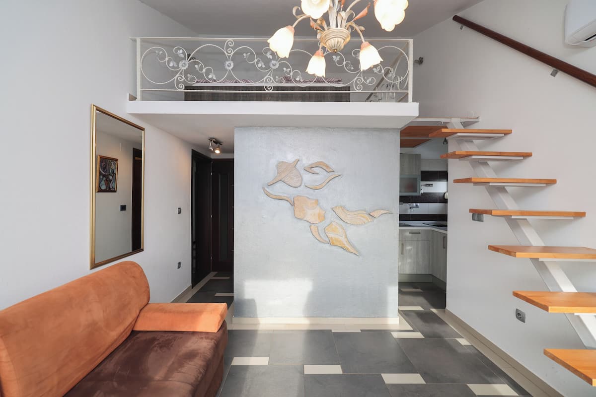 A modern interior with a sofa, a decorative wall, a staircase, and a kitchen area.