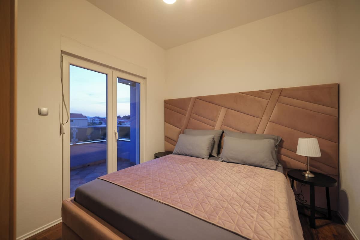 A bedroom with a large bed, a headboard, a nightstand, and a view through a sliding door.