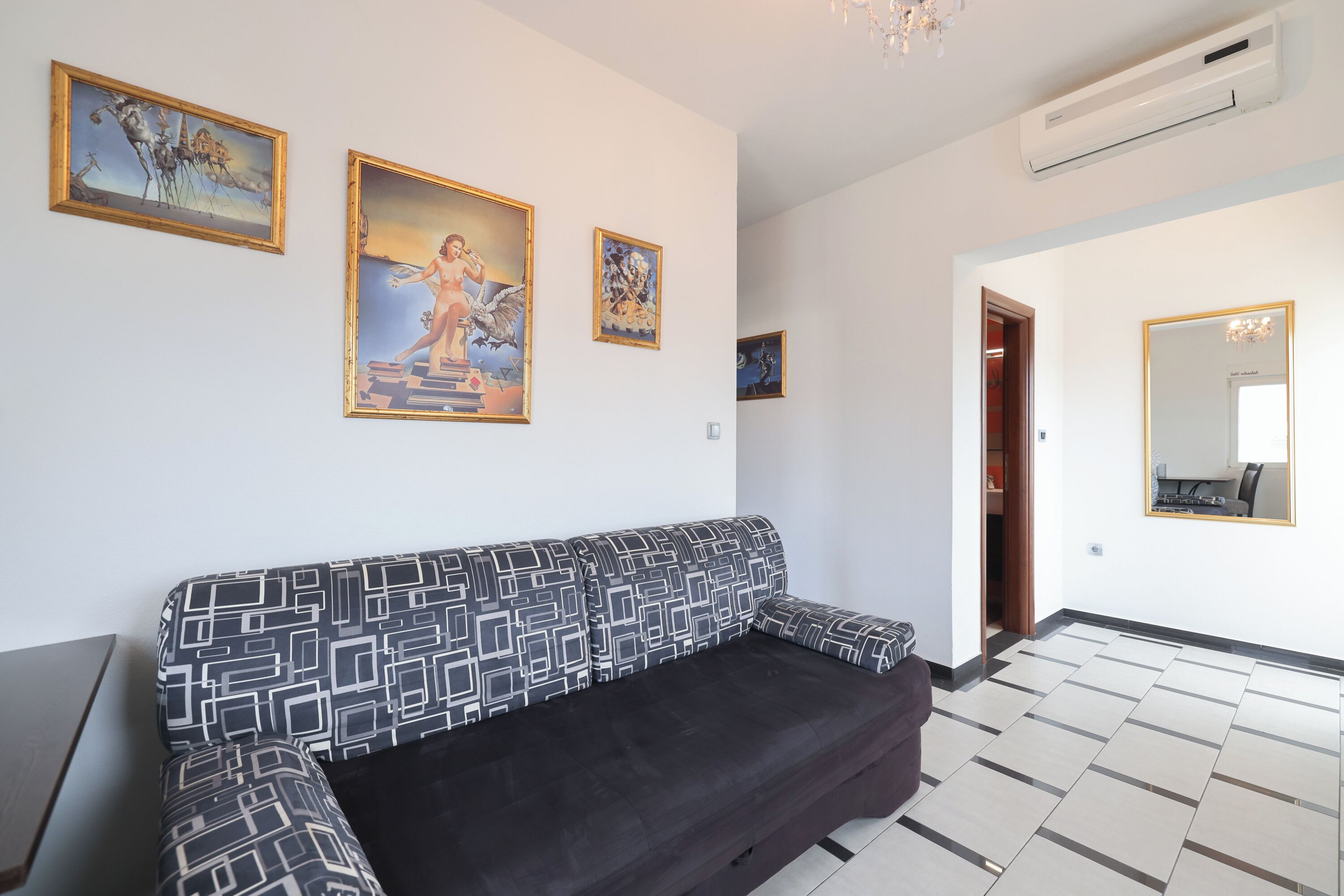 A living room with a patterned sofa, a large mirror, and three framed artworks on the wall.