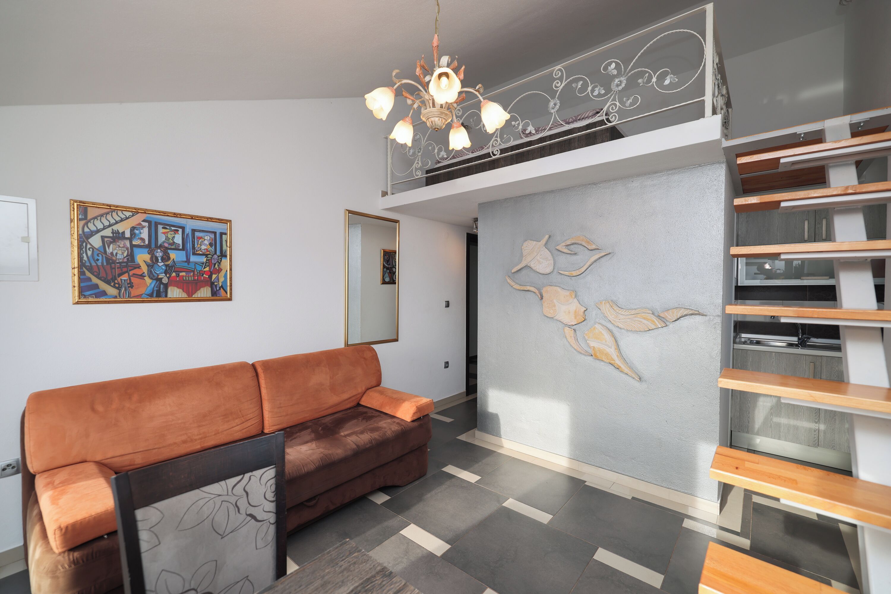 A modern living room with a brown sofa, a chandelier, a staircase, and a wall with leaf patterns.