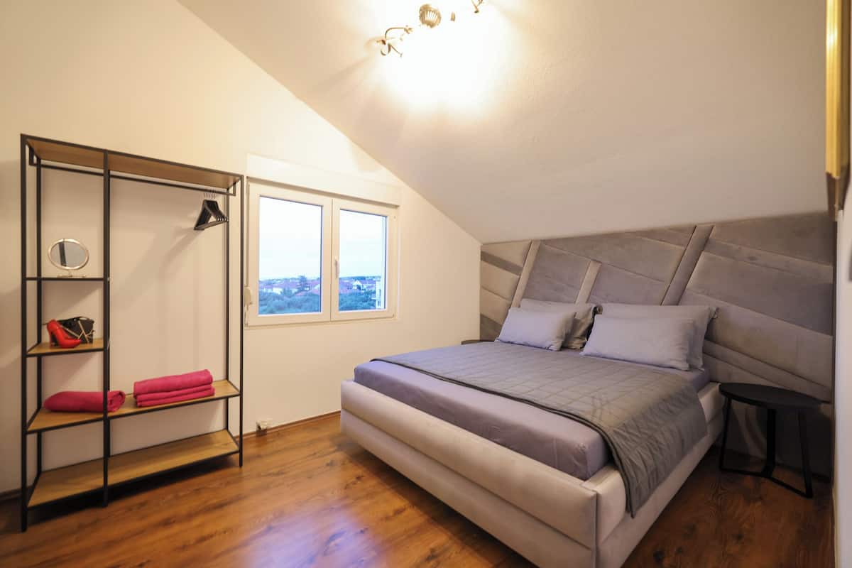 A bedroom with a bed, a wooden floor, a window, and a built-in shelf with towels.