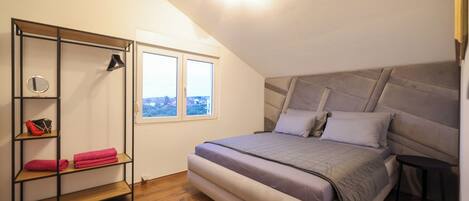 A bedroom with a bed, a wooden floor, a window, and a built-in shelf with towels.