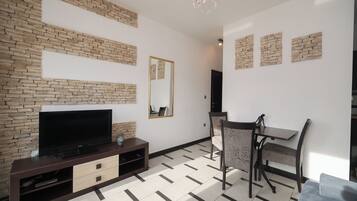 A modern living room with a flat-screen TV on a dark wooden entertainment unit, a dining area with a table and chairs, and a patterned rug on the floor.