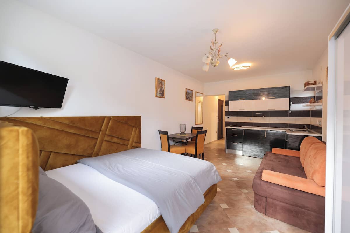 A modern hotel room with a bed, a sofa, a dining table, and a kitchenette.