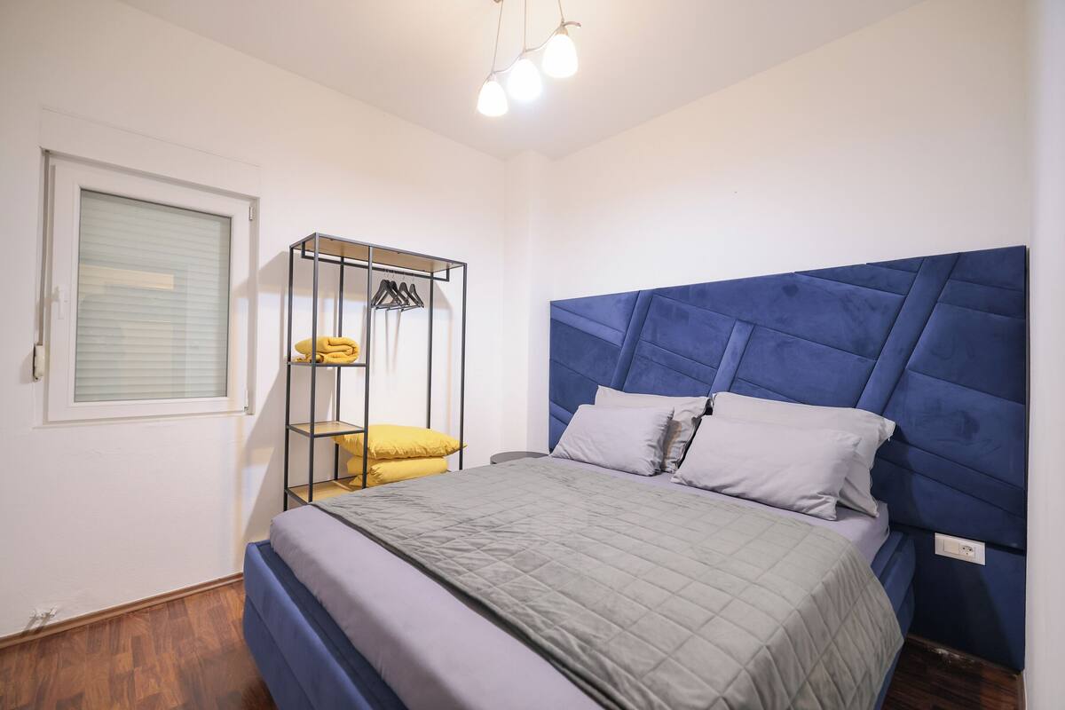A bedroom with a bed, a wardrobe, and a window with blinds.