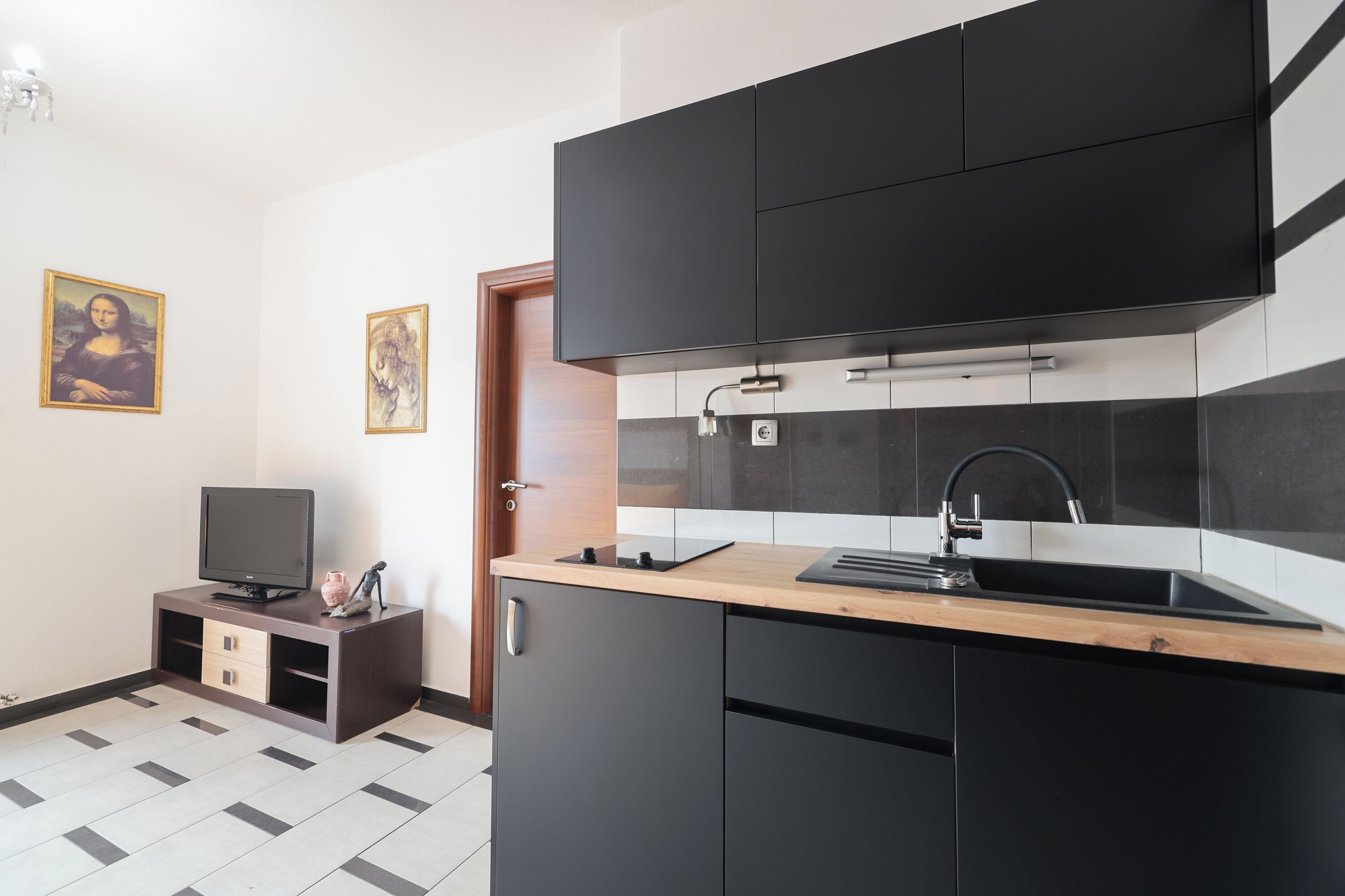 A modern kitchen with black cabinets, a wooden countertop, a built-in sink, and a television on a wooden stand.