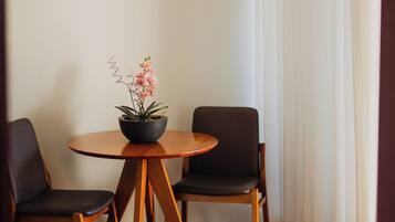 A room with a round wooden table, two chairs, a potted plant, and a white curtain.
