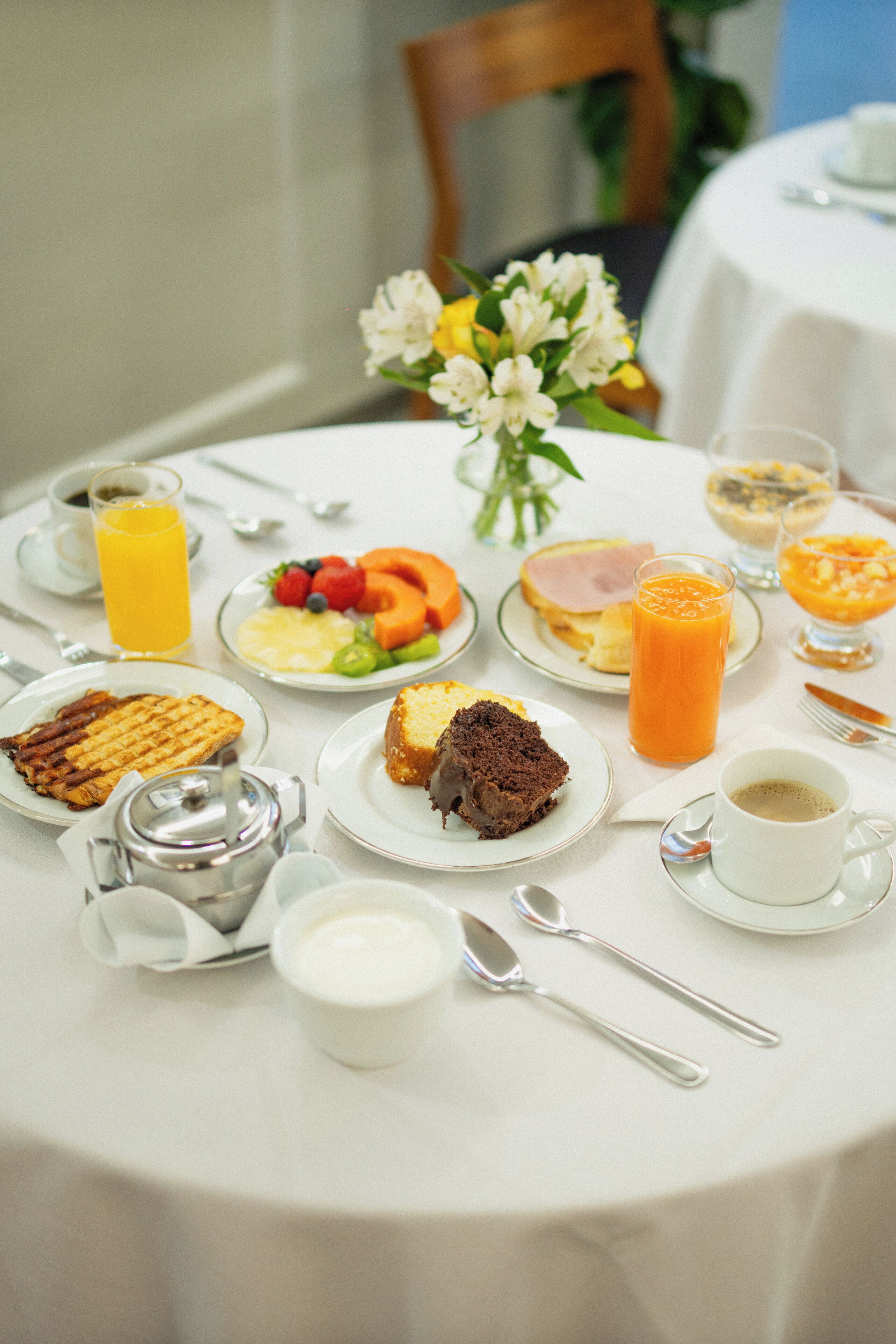 A breakfast table with plates of food, a vase of flowers, and a coffee cup.