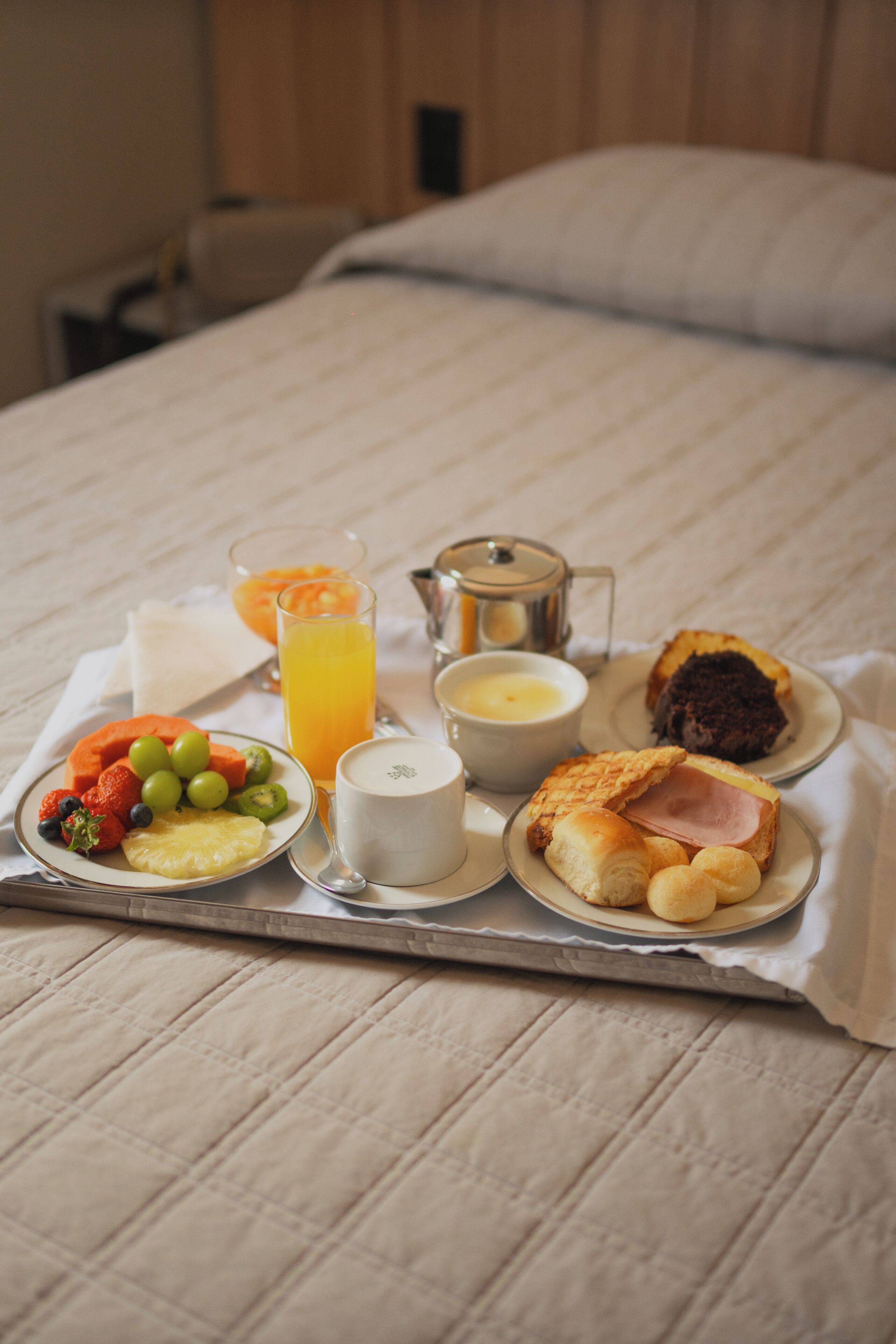 Ein Frühstücksbrett mit Früchten, Saft, Kaffee und Gebäck auf einem Bett.