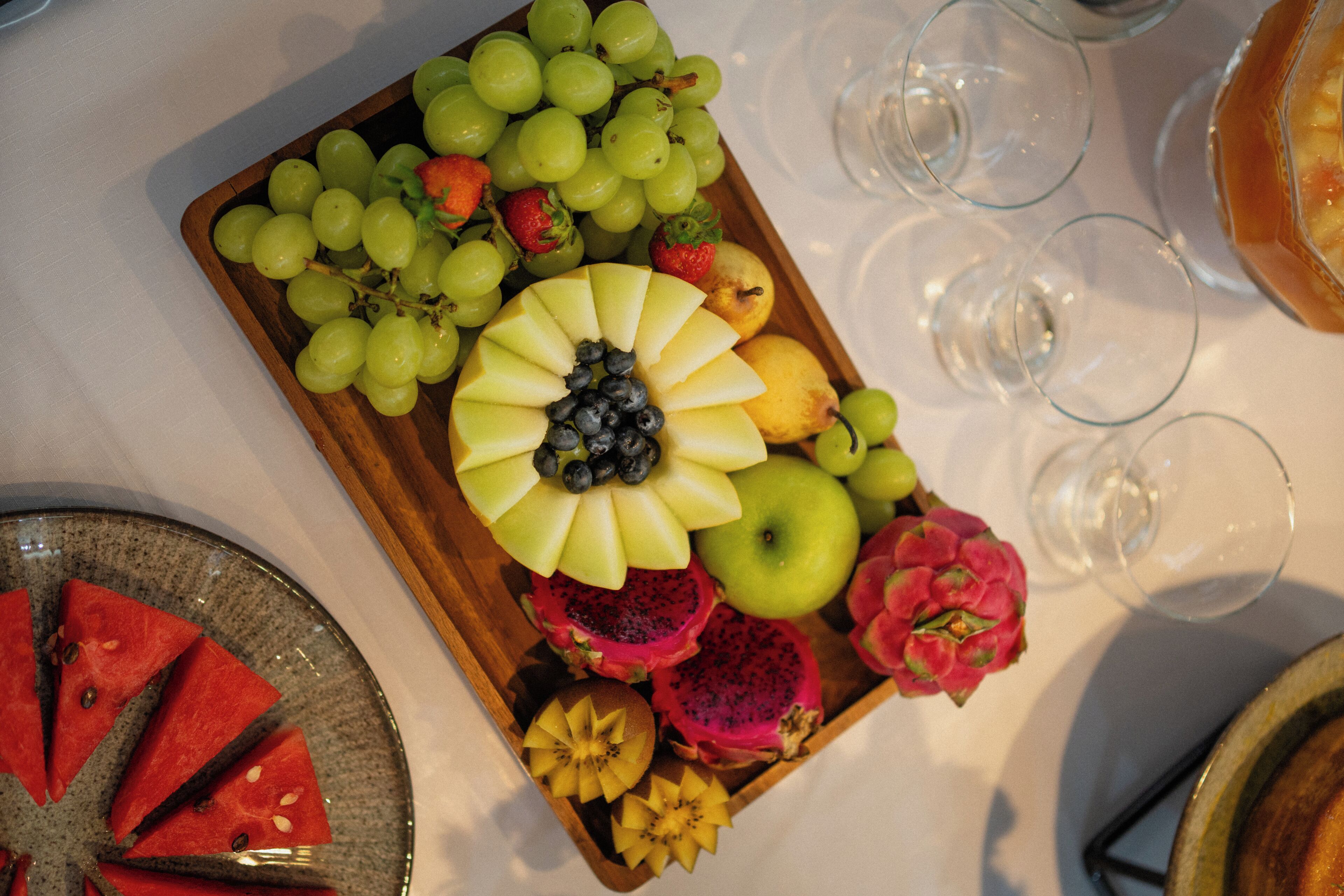 A fruit platter with various fruits and a slice of watermelon on a table.