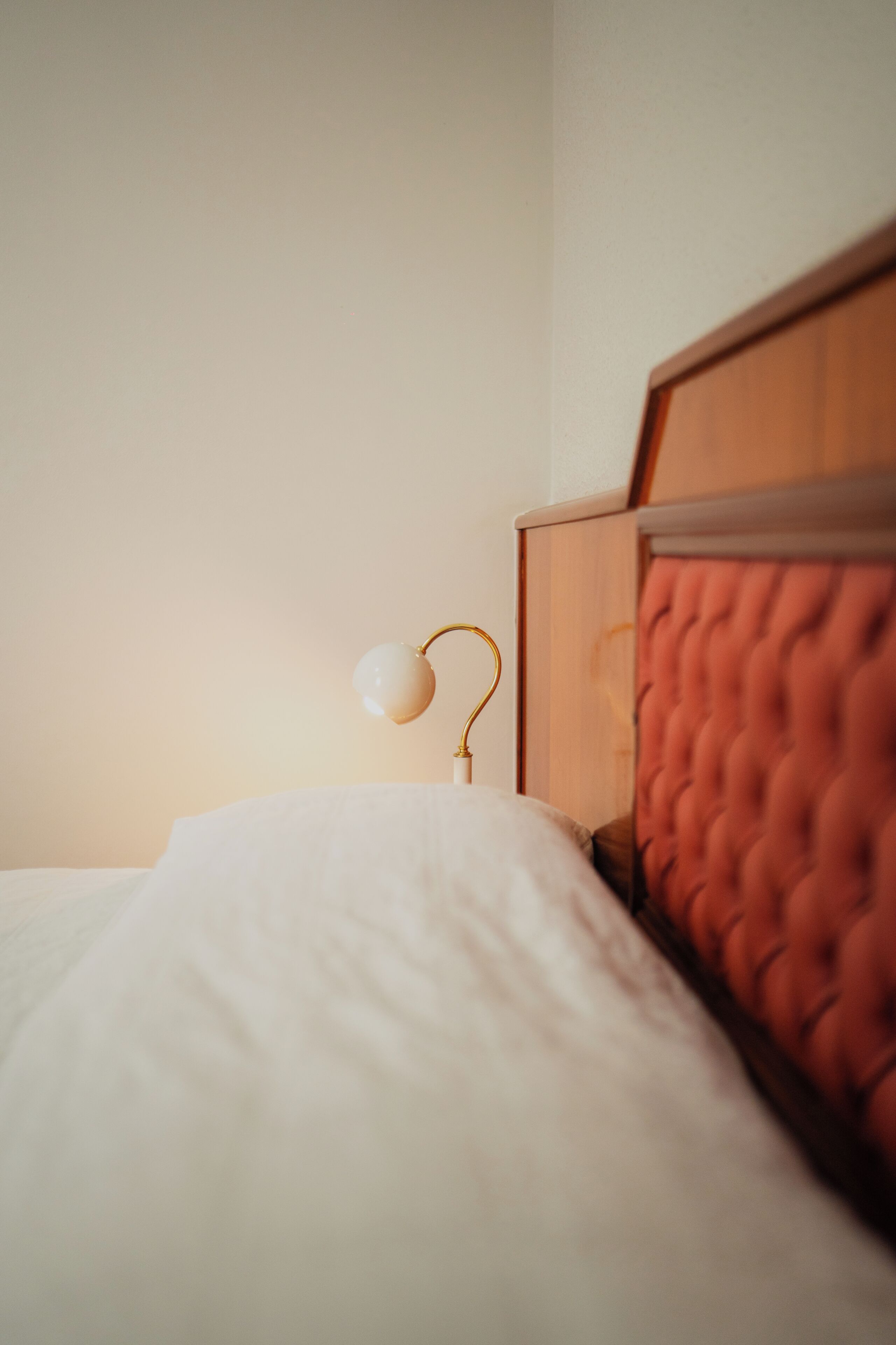A bed with a wooden headboard, a white pillow, and a bedside lamp with a gold base.