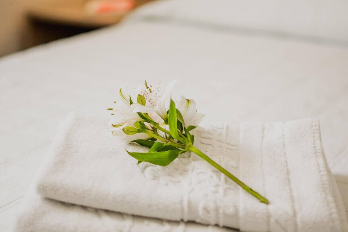 Een keurig opgevouwen witte handdoek met een witte bloem op een bed.