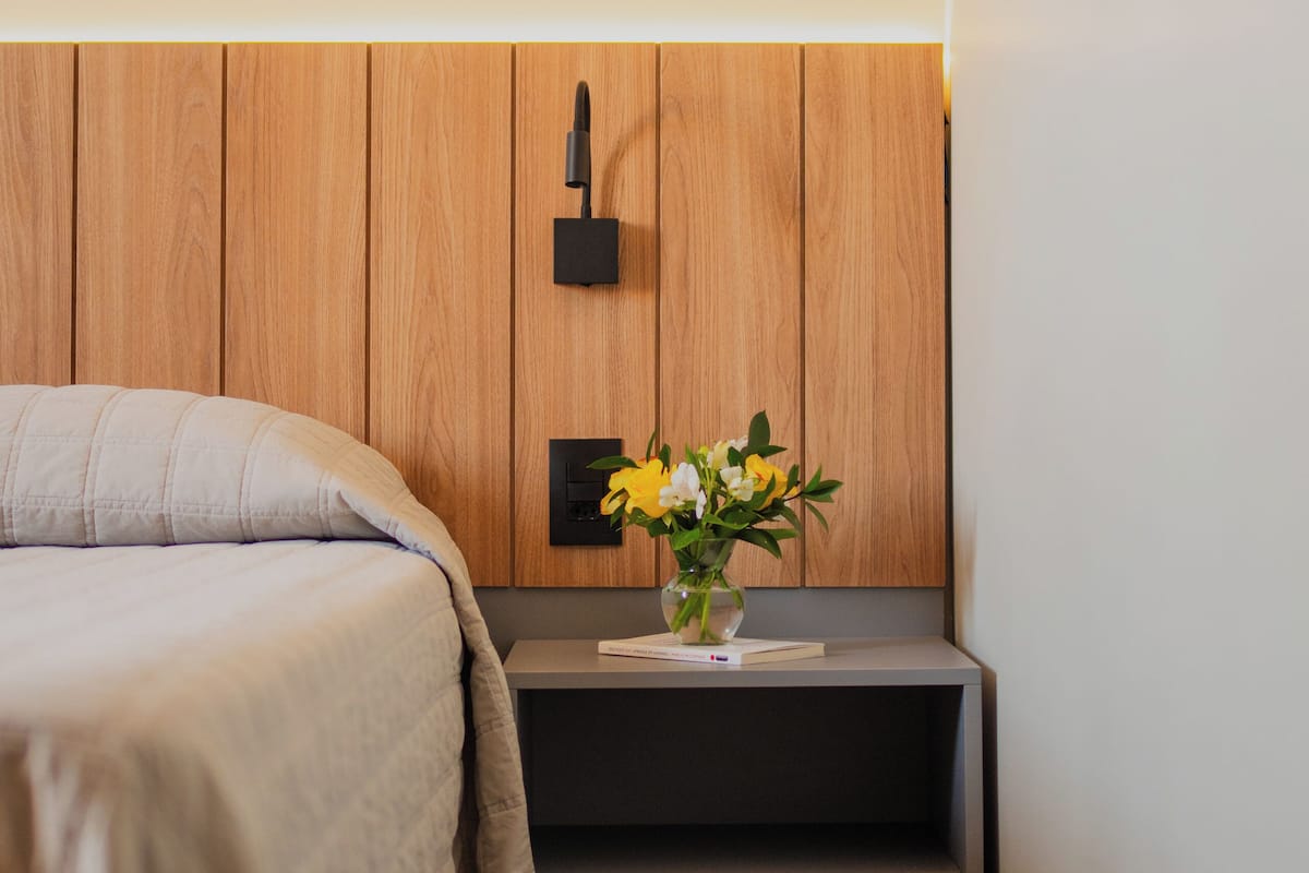 Een slaapkamer met een bed, een nachtkastje met een bloemenvaas en een houten hoofdeinde.