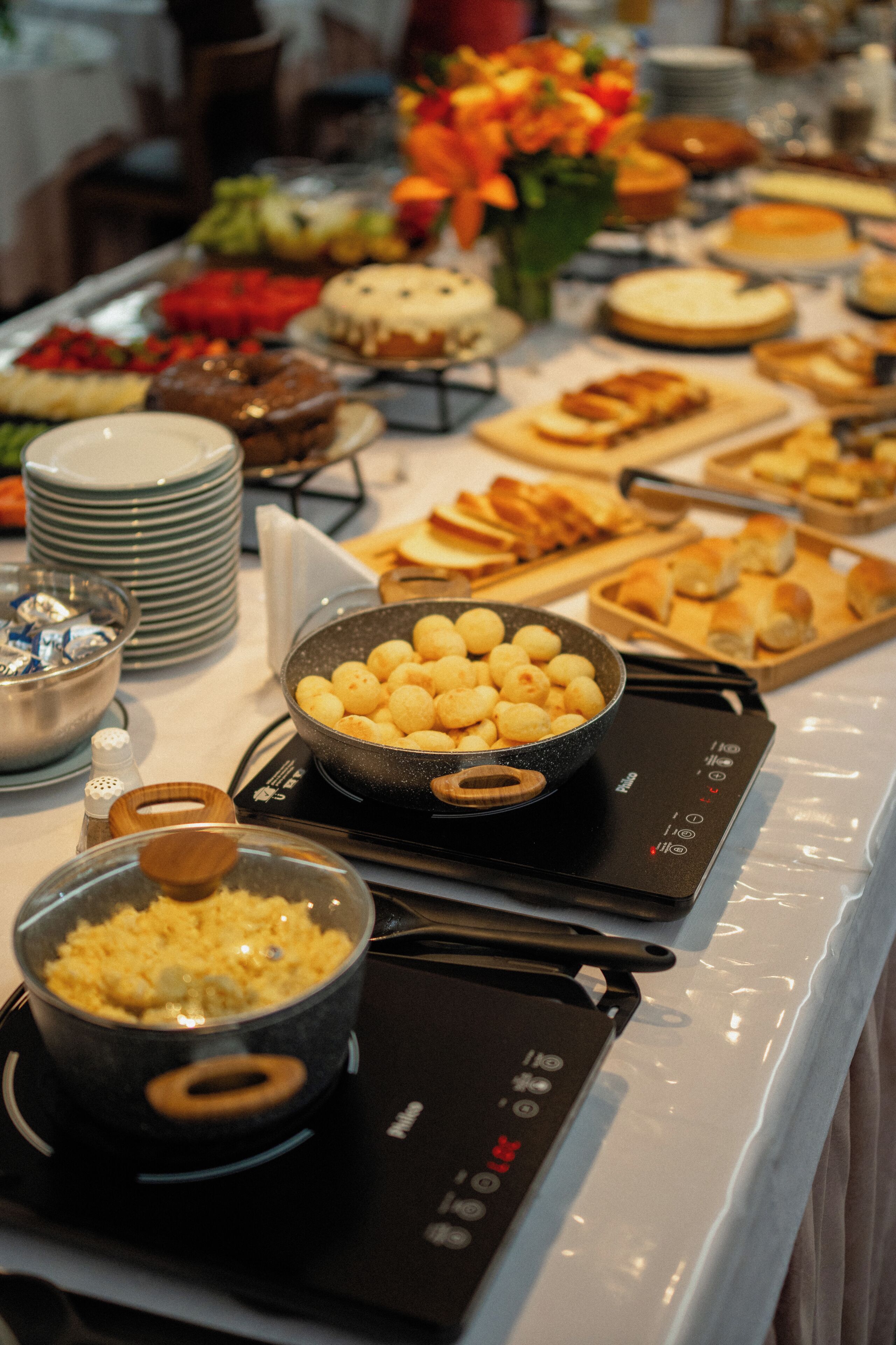 Een buffet met verschillende soorten eten, waaronder een schaal kaasballetjes, een schaal roerei, en verschillende bakplaten met brood en gebak.