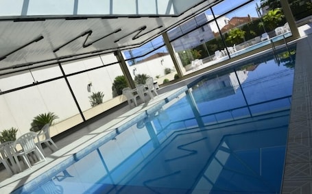 Una piscina techada, una piscina al aire libre, sombrillas