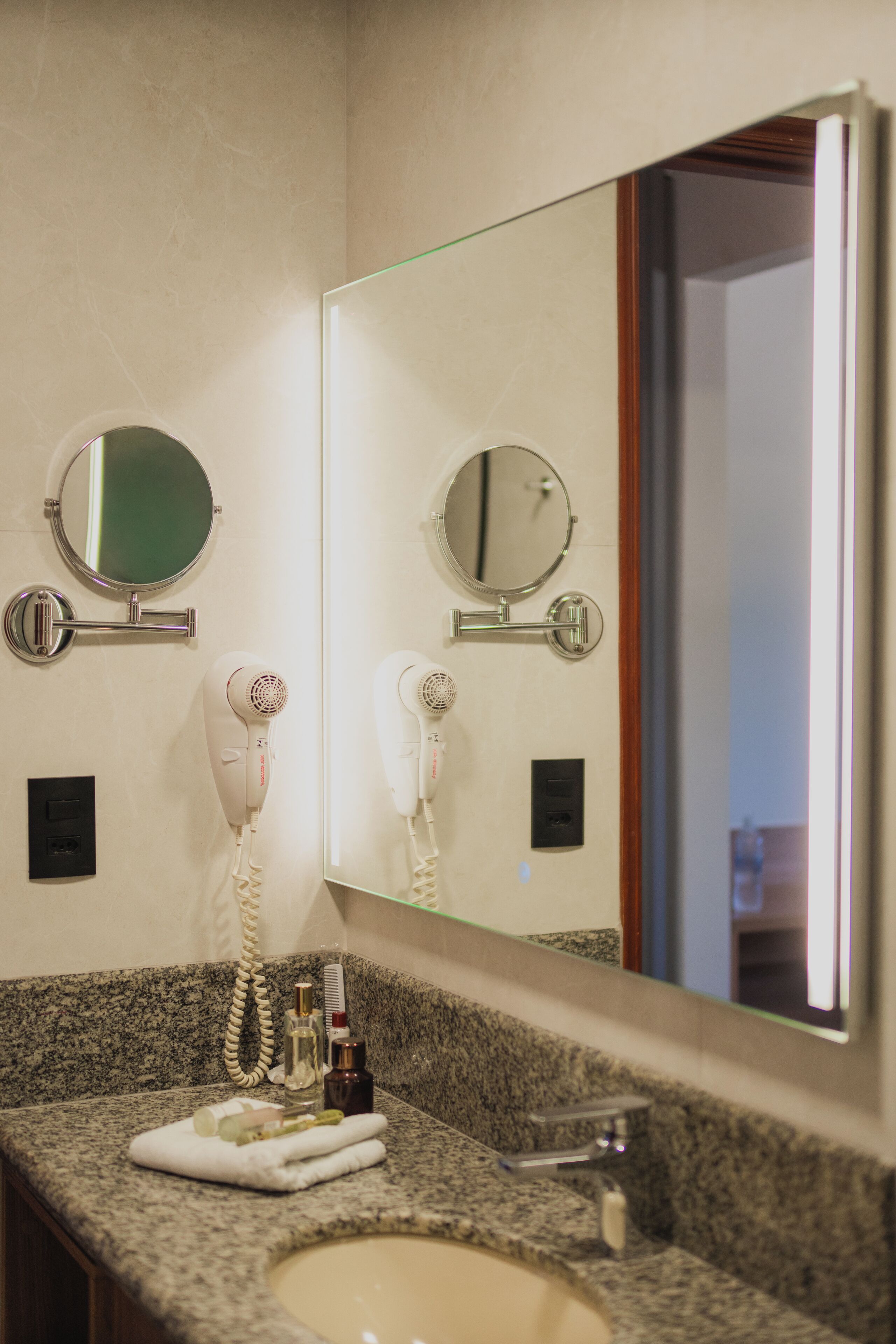 A bathroom with a granite countertop, a sink, a mirror, two hair dryers, and a towel.