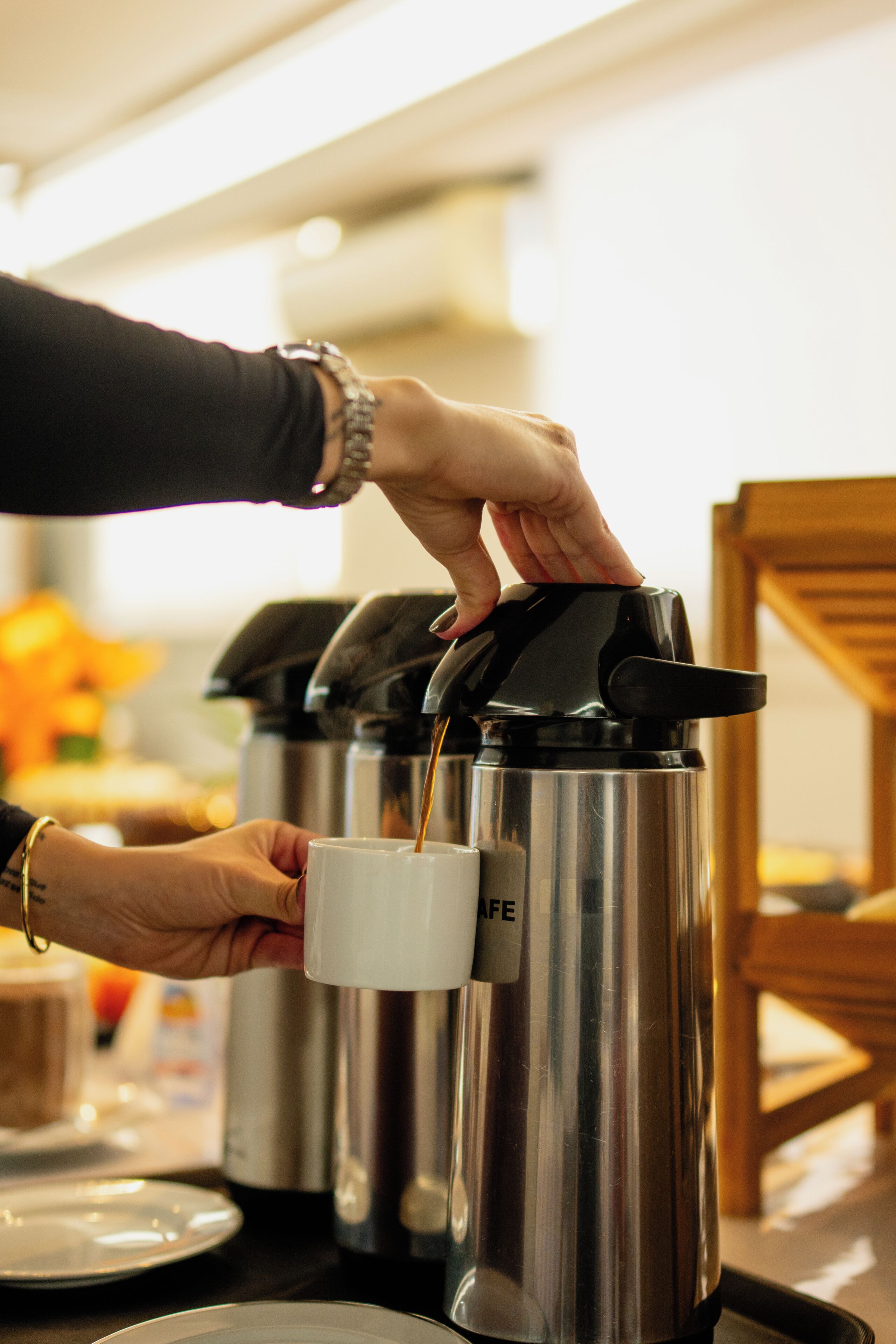 Una persona sirve café desde una cafetera de acero inoxidable en una taza blanca.