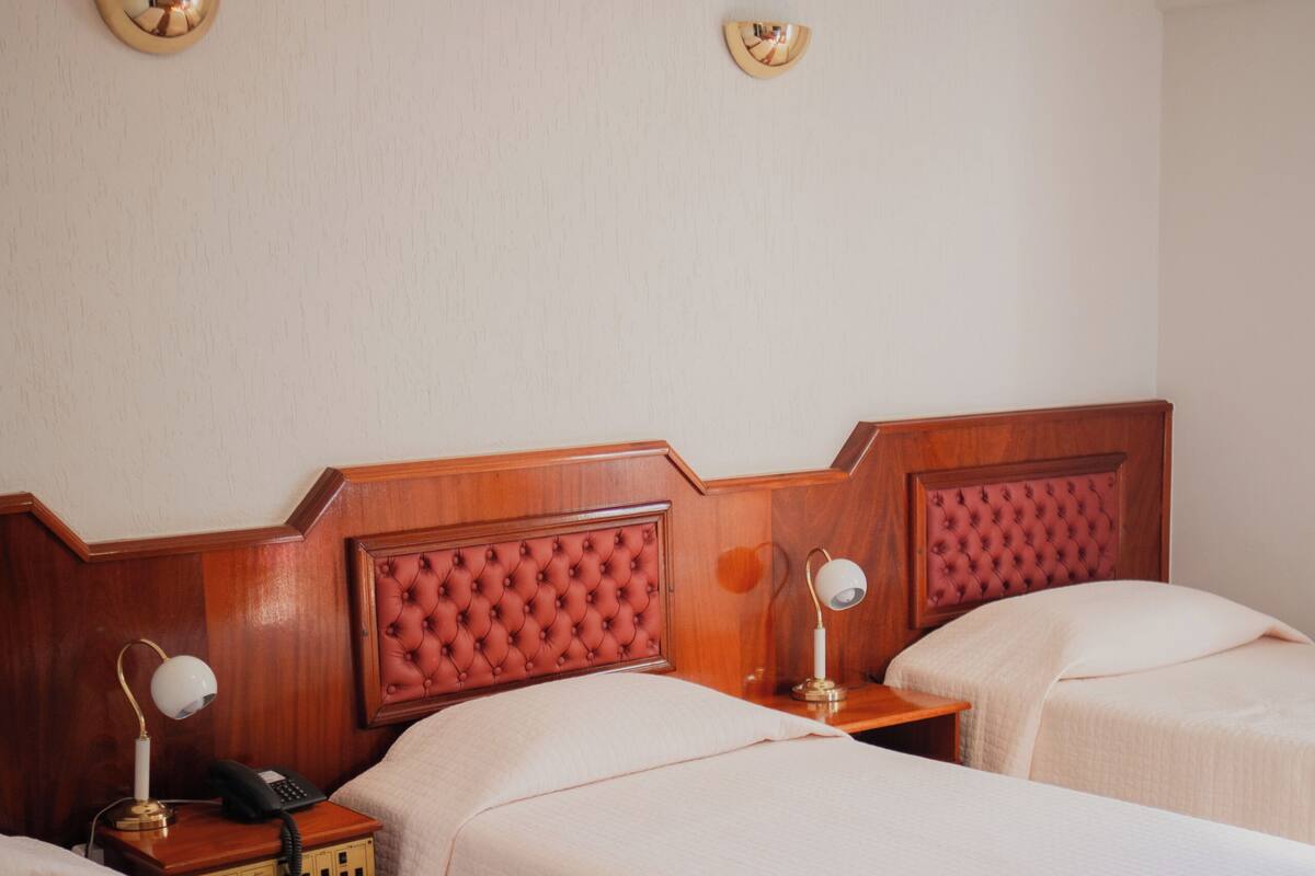 Een hotelkamer met twee bedden, een houten hoofdbord, nachtkastjes met lampen, en een wandlamp.