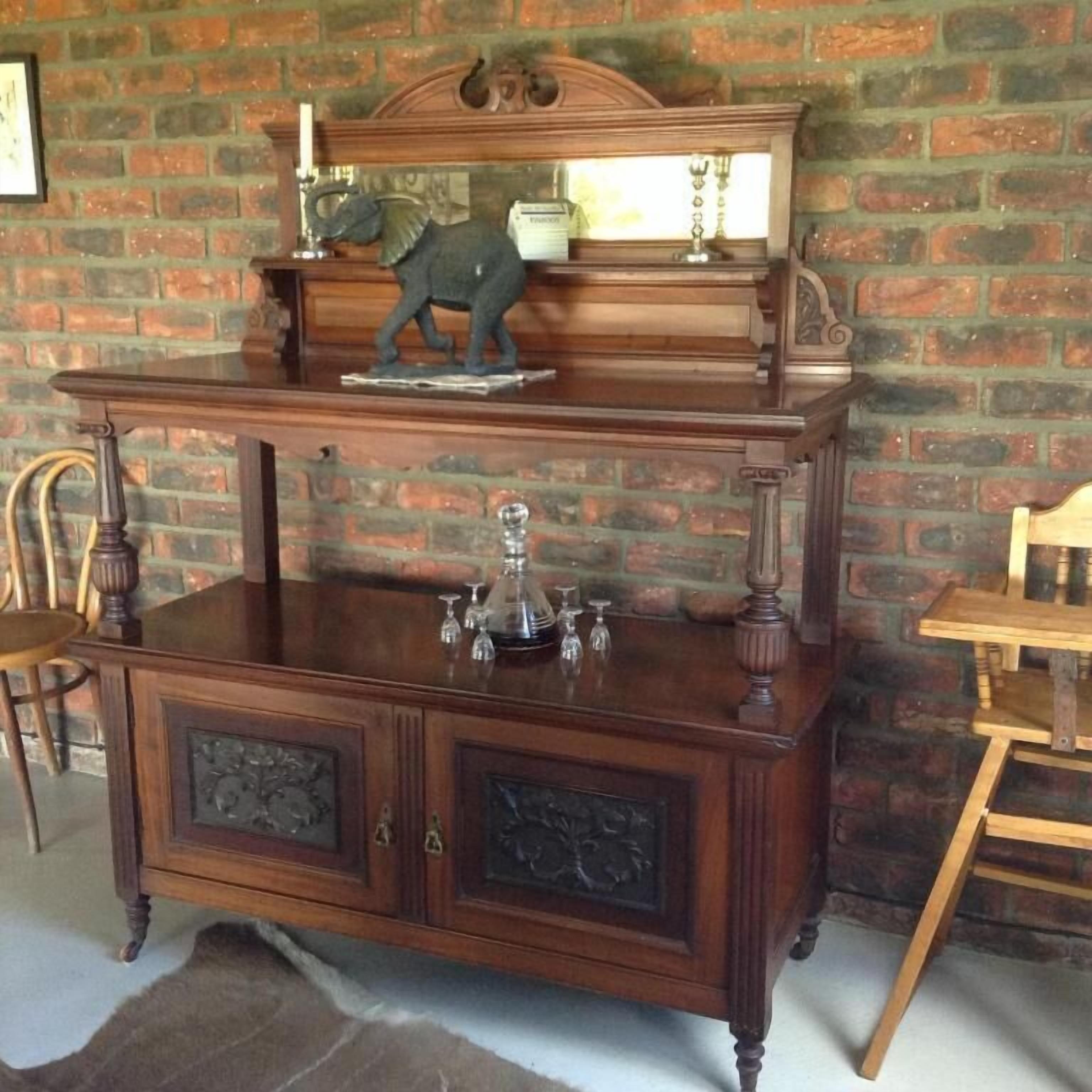 A wooden piece of furniture with a mirror, a decorative plate, and a glass set.