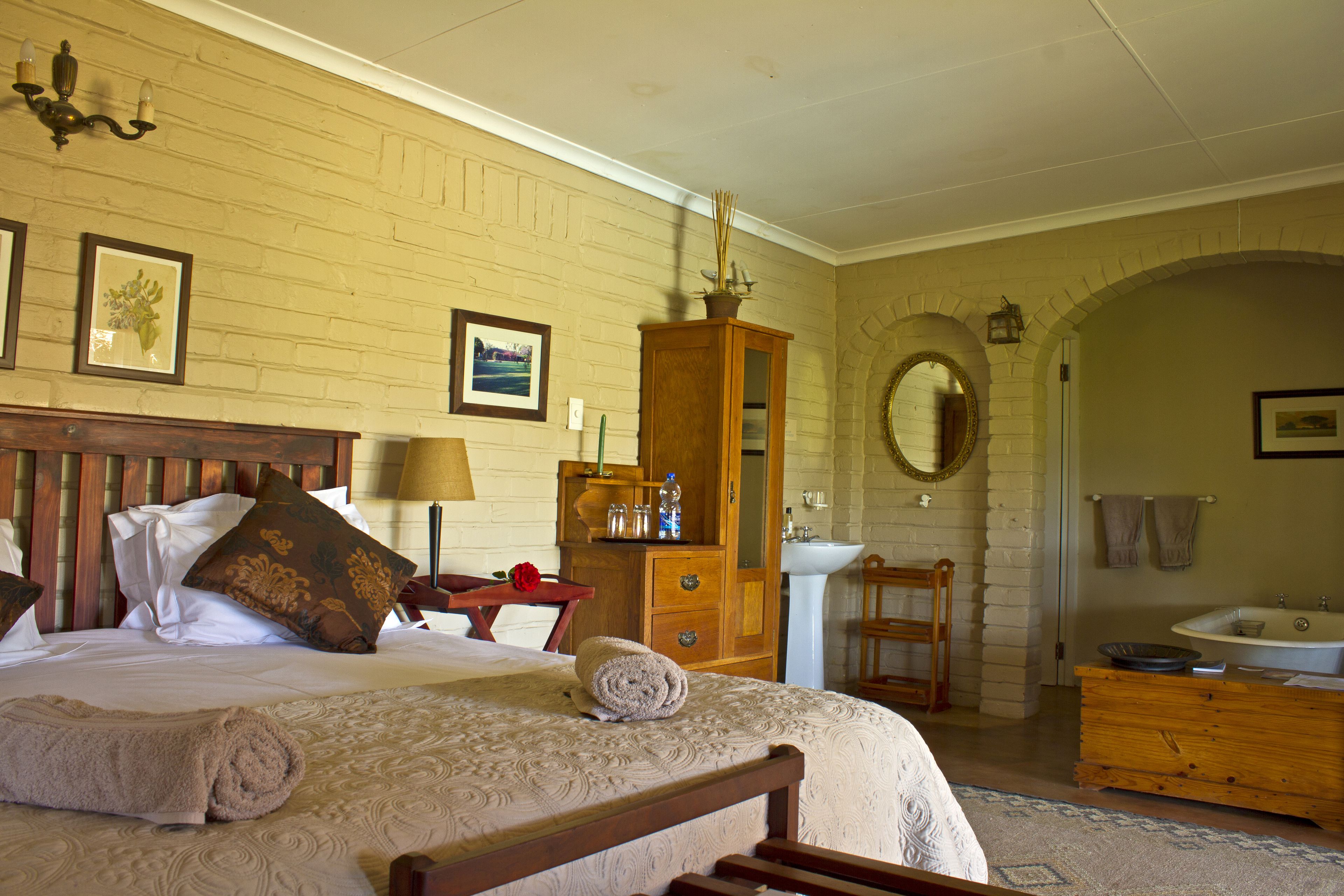 Une chambre d’hôtel comprenant un lit, une tête de lit en bois, une commode en bois, un miroir, un lavabo et un meuble-lavabo dans la salle de bain.