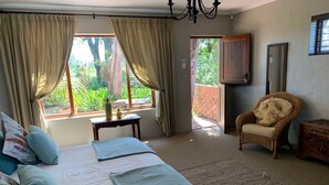 A bedroom with a bed, a chair, a small table, and a view of the outdoors.