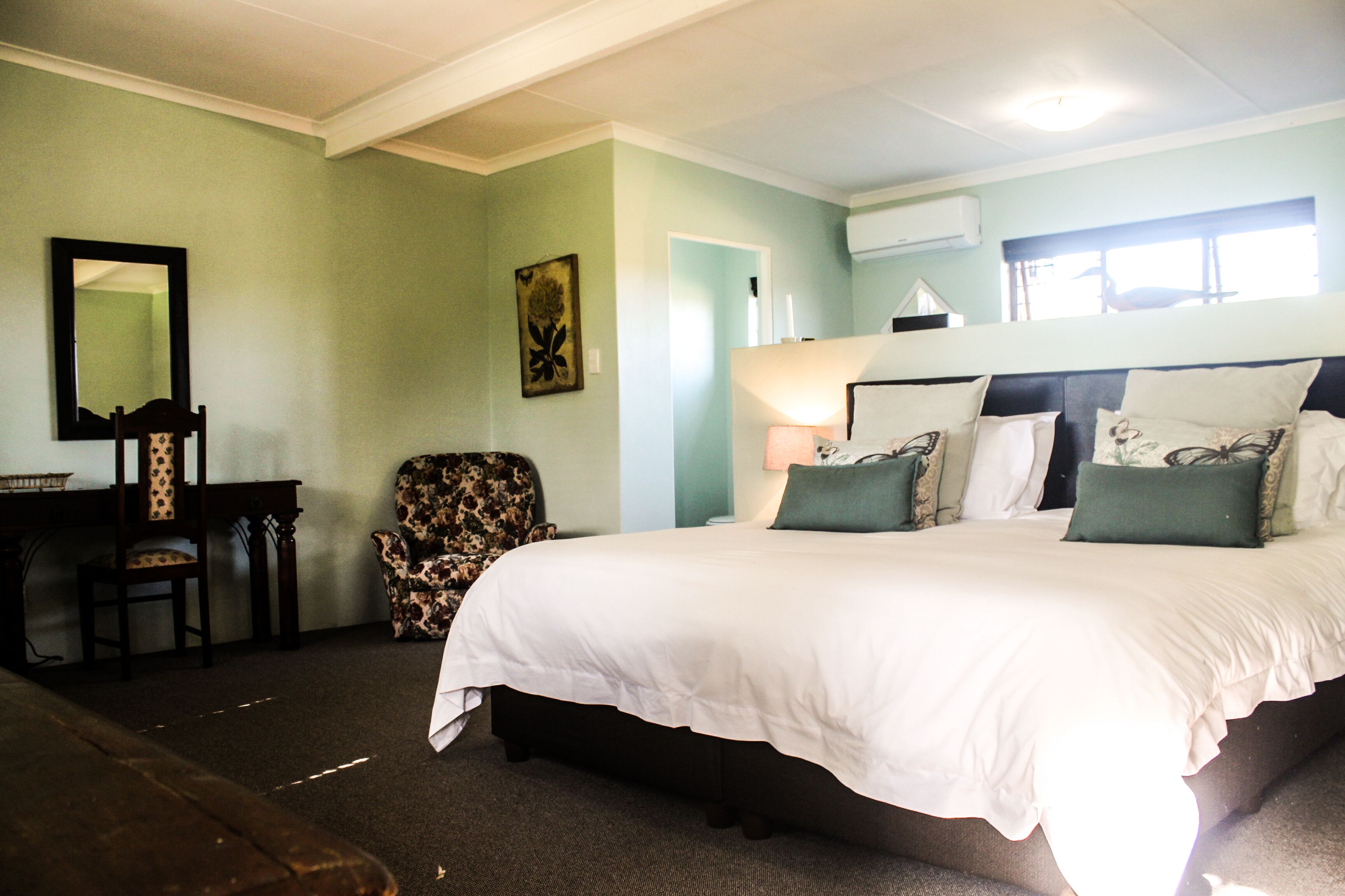 A bedroom with a large bed, a chair, a desk, and a mirror.
