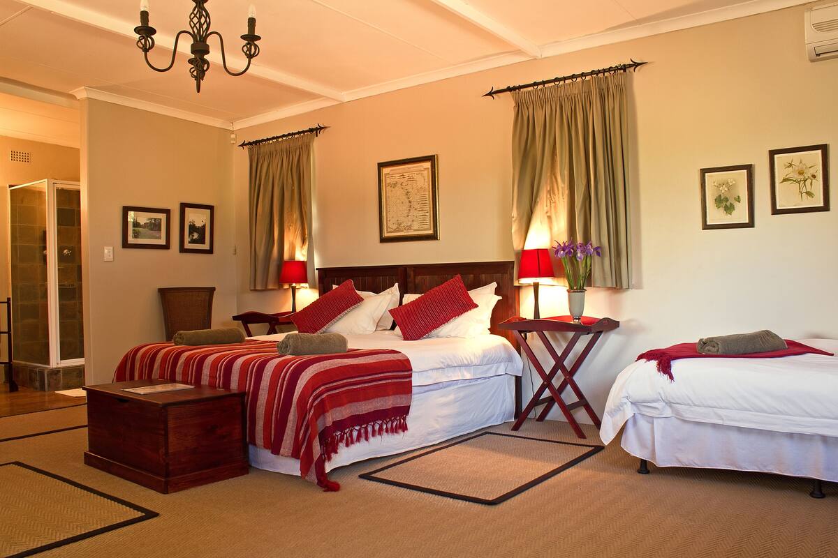 A hotel room with two beds, a wooden headboard, a red and white striped blanket, a wooden nightstand, a red lamp, and a framed map on the wall.