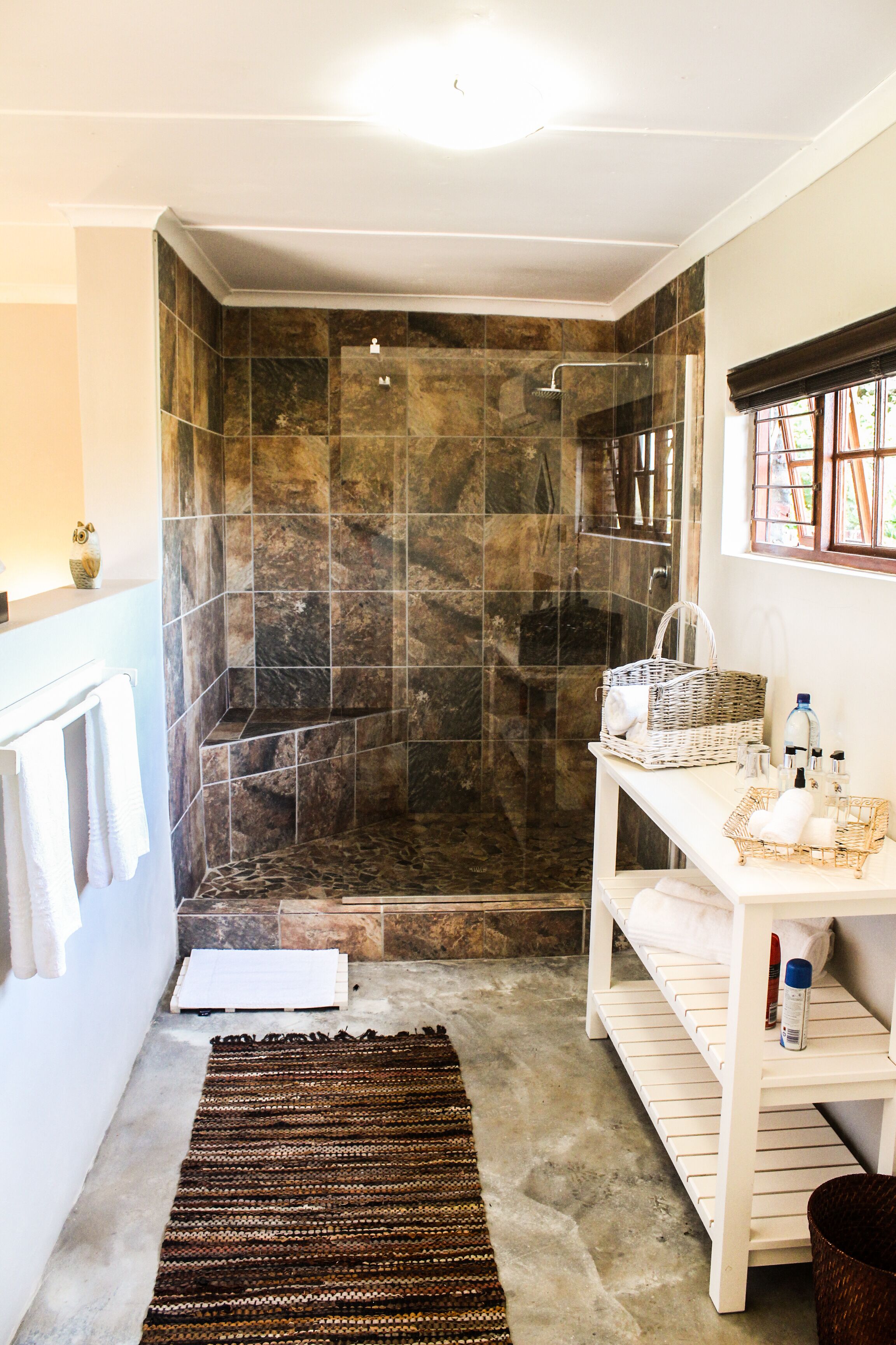 A bathroom with a shower, a white sink with a basket, and a towel rack.