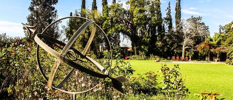 Un jardín con una escultura de metal, césped y árboles altos.