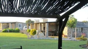 Un espacio al aire libre con techo, una estructura de pérgola, un edificio de piedra y un césped cuidado.