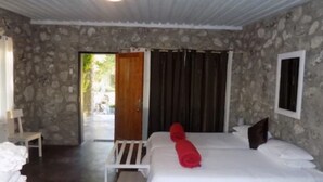 Un dormitorio con pared de piedra, una cama con ropa blanca, una toalla roja y una puerta de madera que da al exterior.